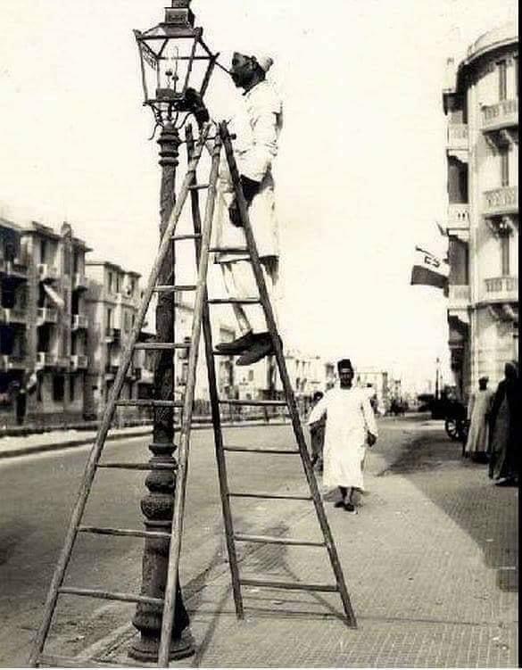 المشعَلجي يُنير أعمِدة الإنَارهـ فِي احد الشَوارع الرَئيسيهـ بِالاسڪَندرية عَام ١٩١٠